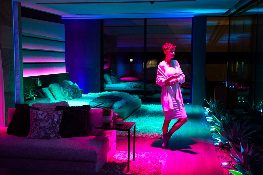 A woman in a bedroom lit with blue-green, purple, and magenta LED lighting.