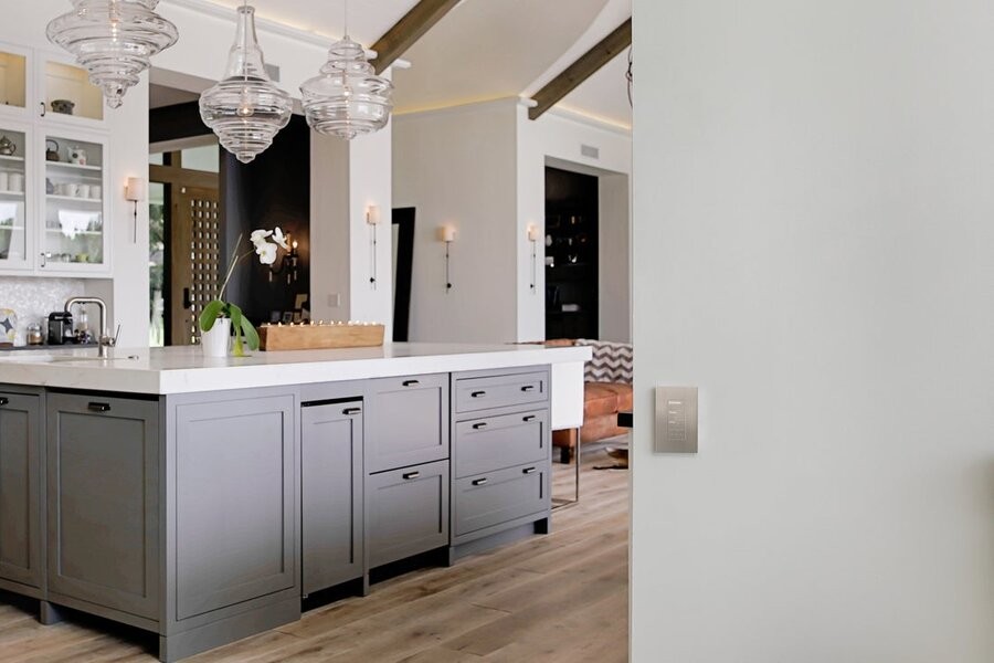 A kitchen space with smart lighting control fixtures and a lighting control switch in the foreground on the wall.