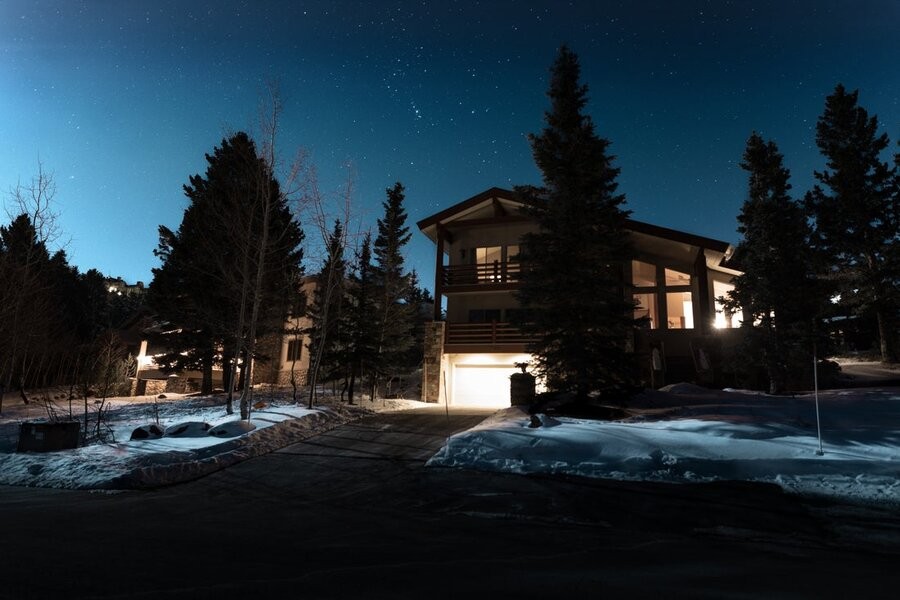 A snowy home exterior at night, the interiors are illuminated.